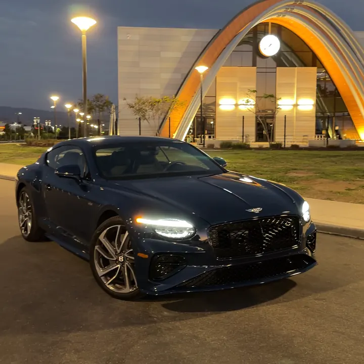 Dark blue Bentley coupe at dusk outside a modern building